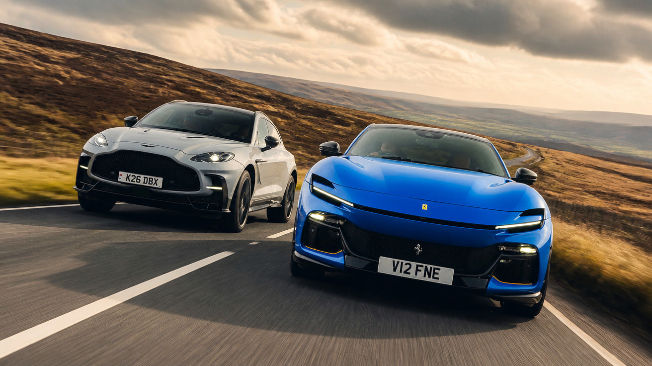 Blauer Ferrari und graues SUV fahren nebeneinander auf einer Landstraße in hügeliger Landschaft bei bewölktem Himmel.