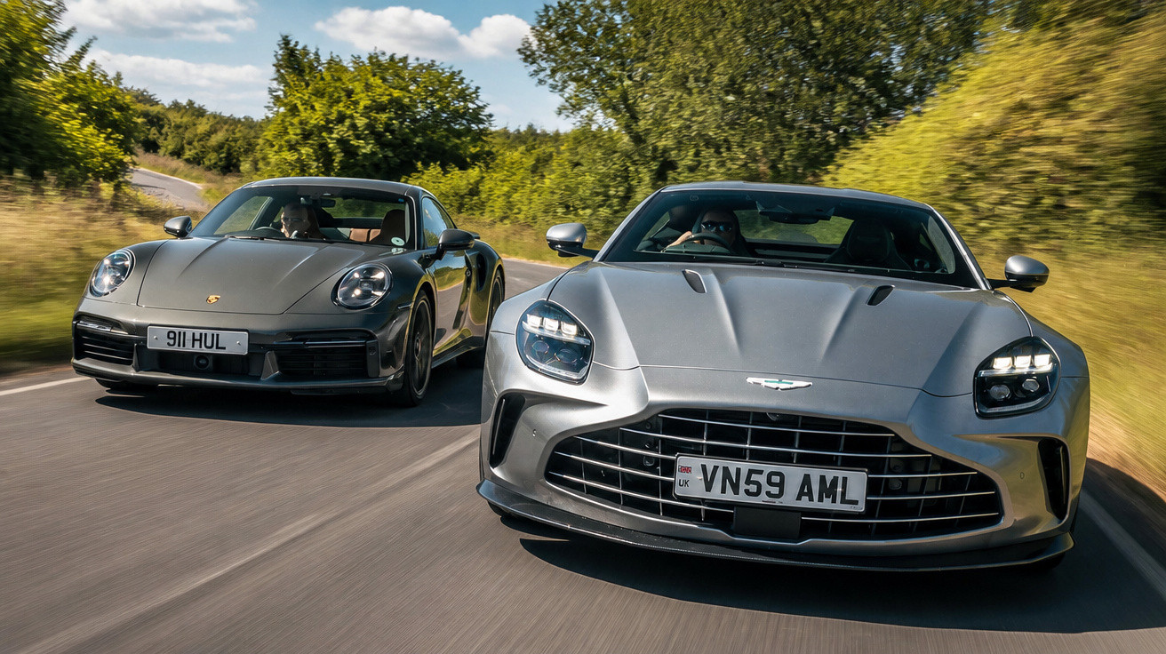 Zwei silberne Sportwagen, ein Porsche und ein Aston Martin, fahren auf einer Landstraße mit Bäumen im Hintergrund.