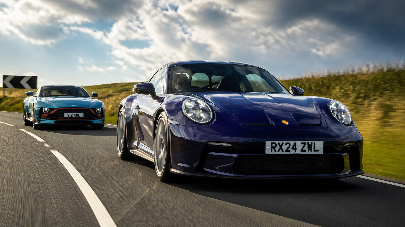 Zwei Sportwagen, ein dunkelblauer Porsche 911 und ein grüner Aston Martin, fahren auf einer Landstraße bei bewölktem Himmel.