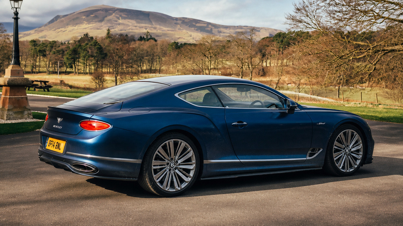 Blauer Bentley Continental GT geparkt auf Asphaltstraße vor bergiger, herbstlicher Landschaft und Bäumen.