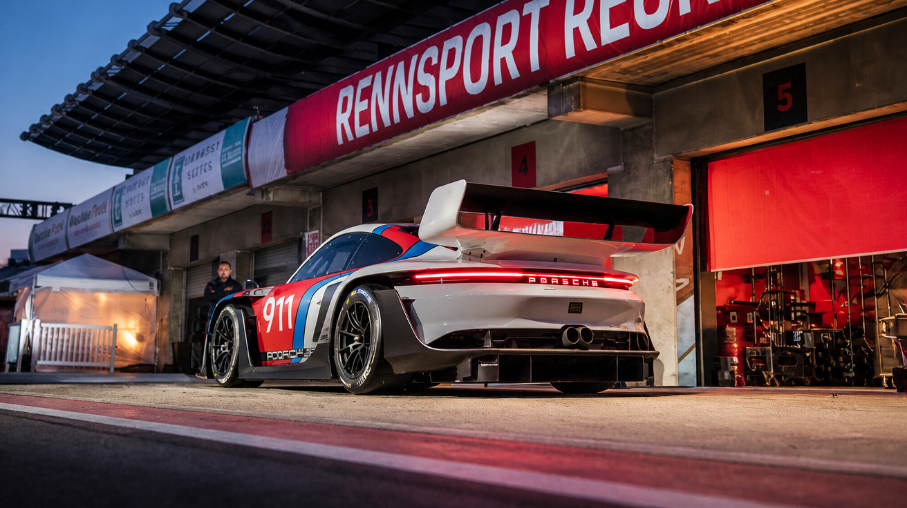 Rennsport-Porsche 911 mit großer Spoiler im Boxenstopp bei Dämmerung vor Rennstall-Garage.