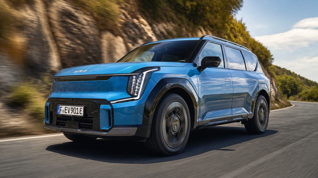 Blaues Elektro-SUV Kia fährt kurvenreiche Straße entlang felsiger Landschaft bei Sonnenschein.