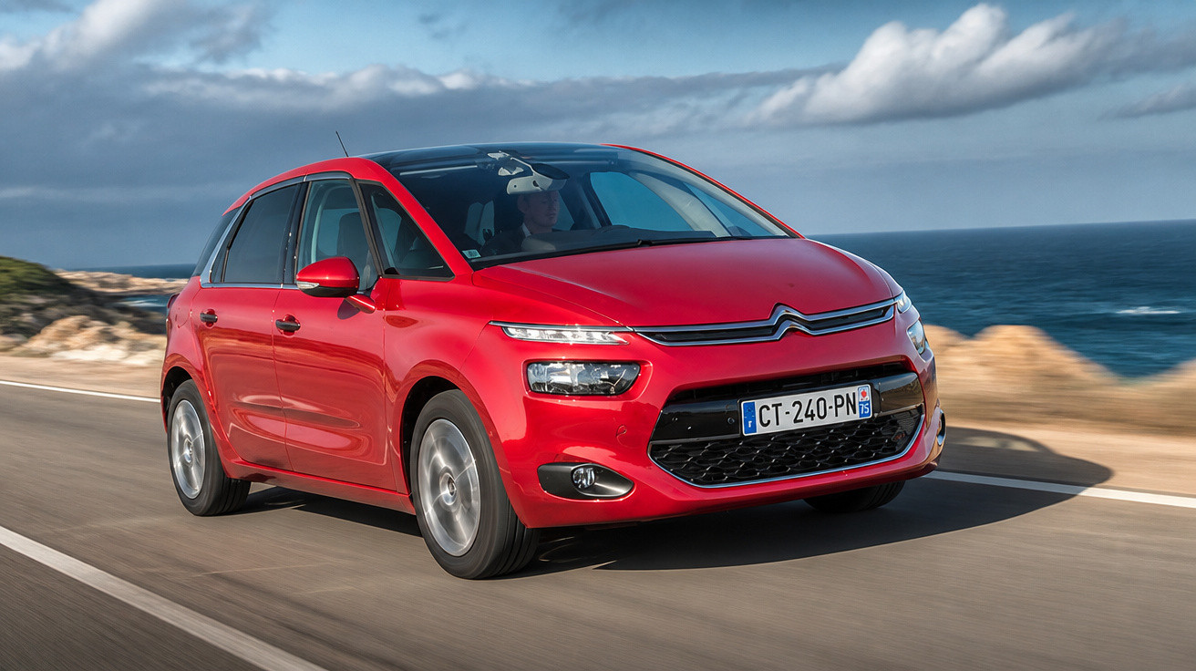 Roter Citroën Kleinwagen fährt auf Küstenstraße bei blauem Himmel und Meer im Hintergrund.