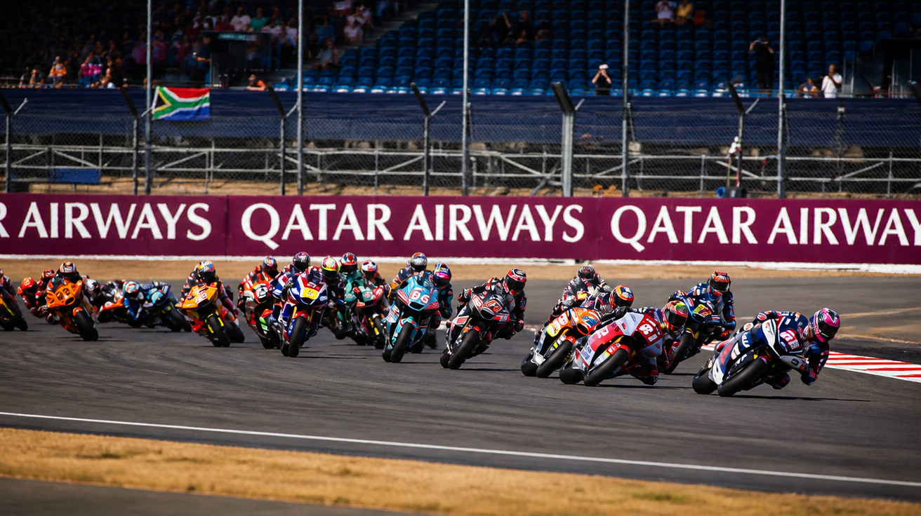 Motorradrennfahrer in voller Montur fahren eng auf einer Rennstrecke mit Qatar Airways Werbebanner im Hintergrund.