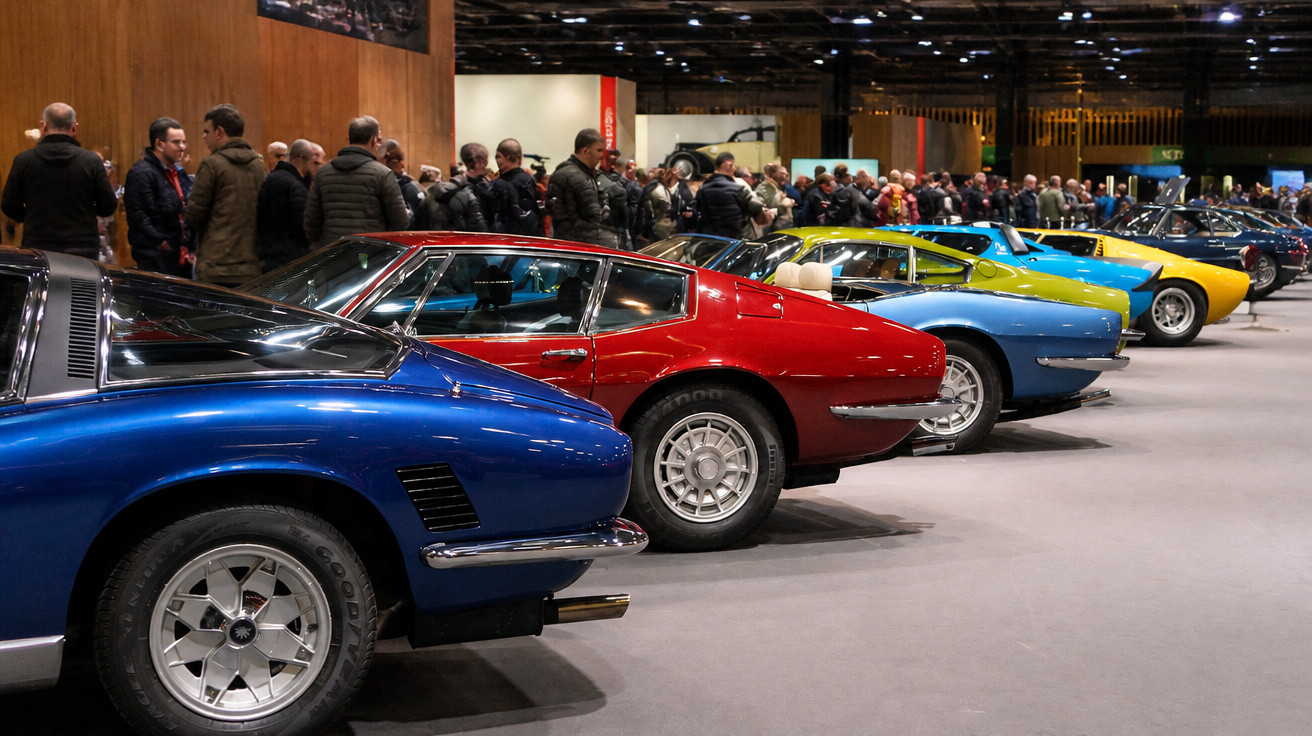 Reihe bunter Oldtimer-Sportwagen bei einer Automesse mit zahlreichen Besuchern im Hintergrund.