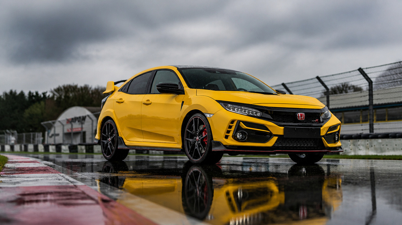 Gelber Honda Civic Type R auf nasser Rennstrecke mit reflektierender Wasserpfütze bei bewölktem Himmel.