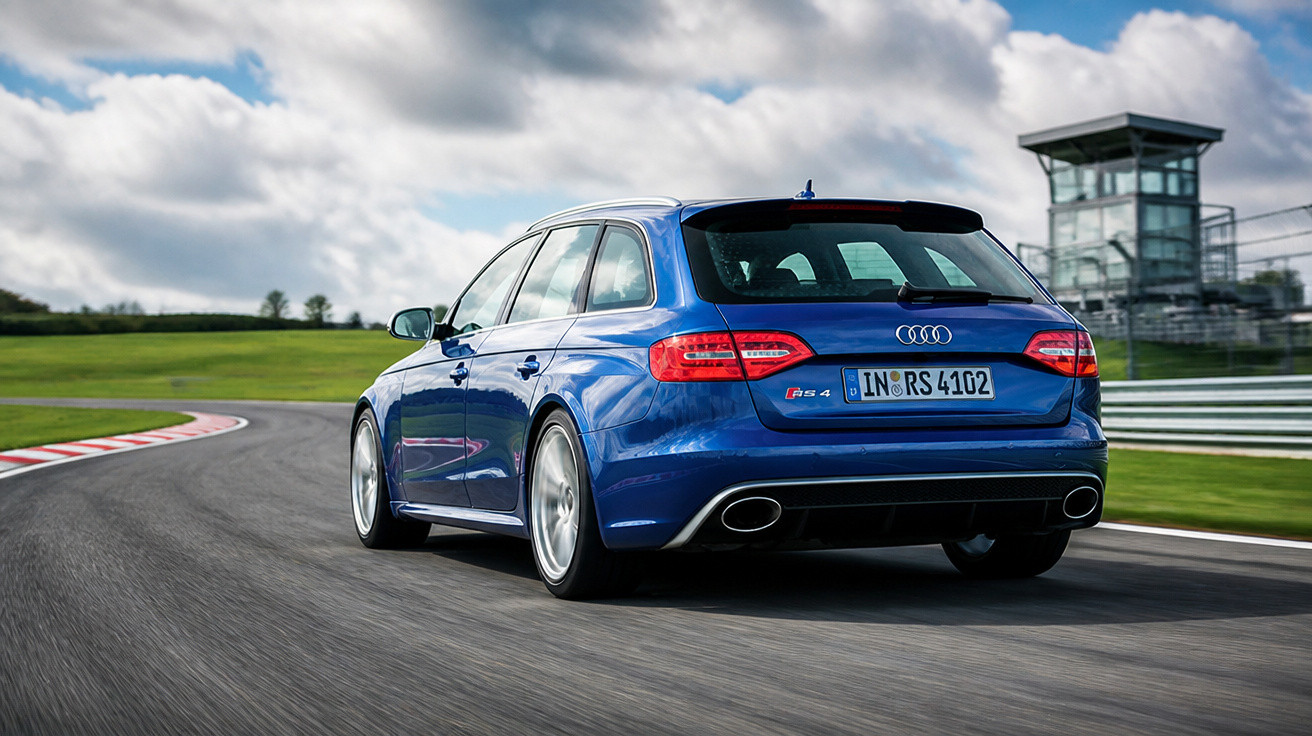 Blauer Audi RS4 Avant fährt auf Rennstrecke bei bewölktem Himmel an Kontrollturm vorbei.