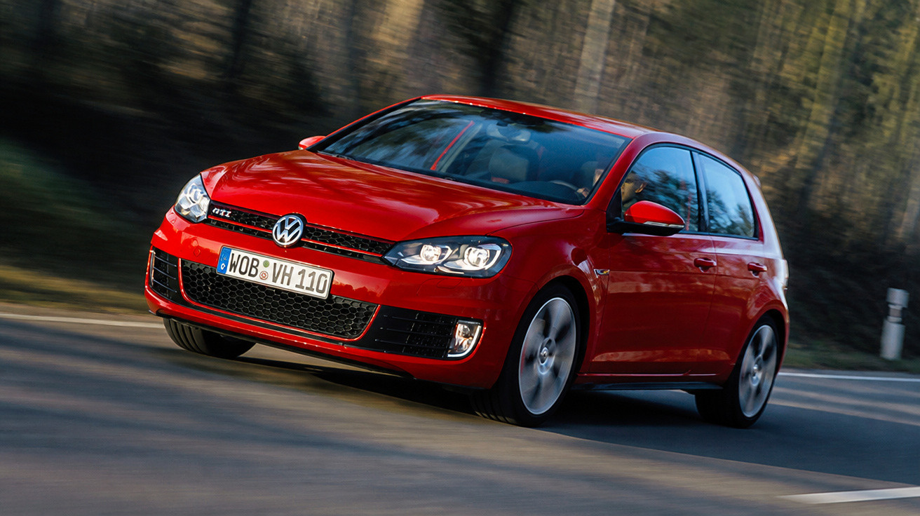Roter Volkswagen GTI fährt auf kurviger Landstraße, Wald im Hintergrund.