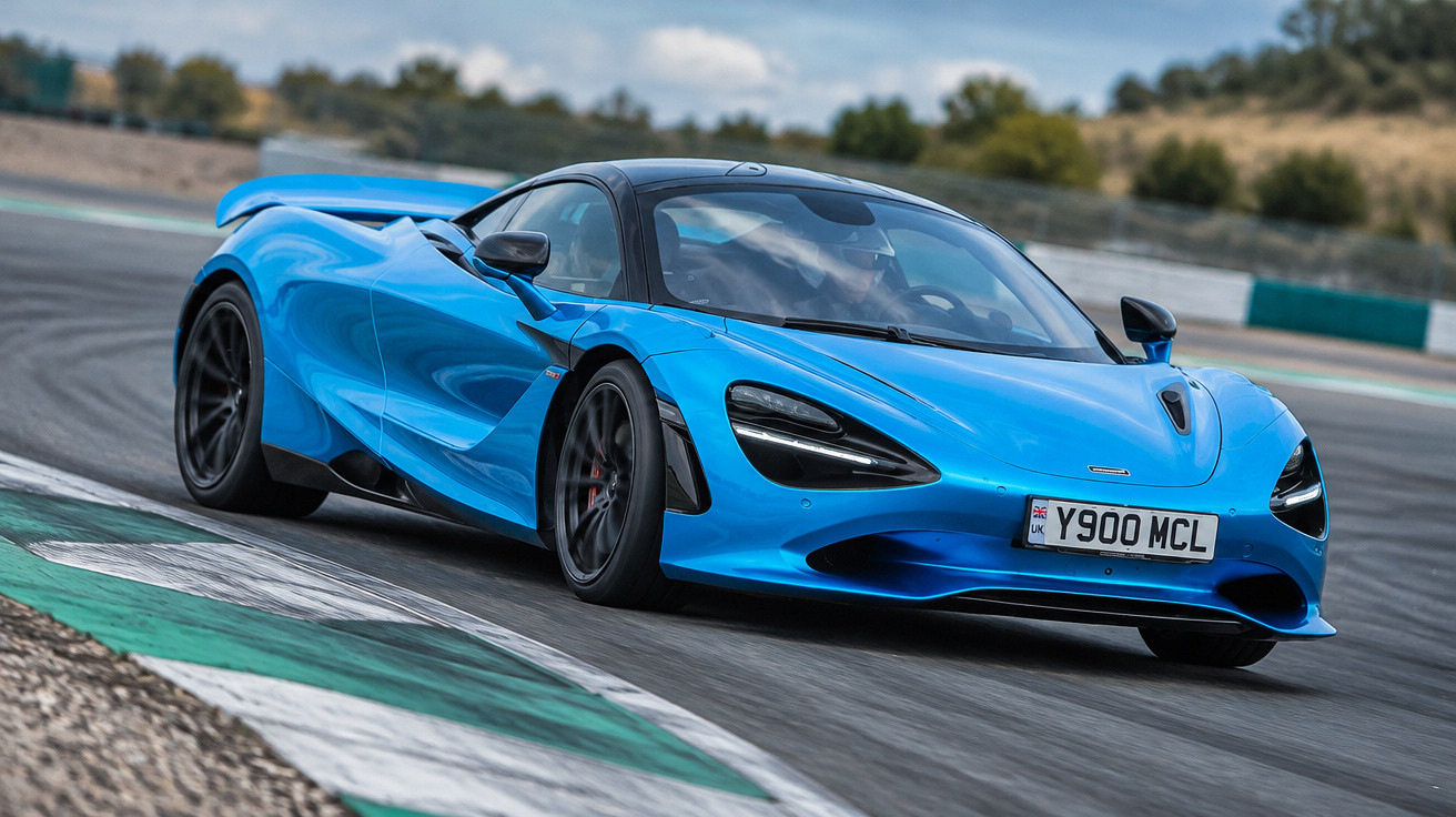 Blauer McLaren Sportwagen fährt auf Rennstrecke in Kurve bei bewölktem Himmel.